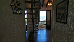 A narrow hallway with wooden flooring leading to a balcony with a view of the ocean.