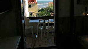 A room with a view of the sea, a balcony with a table and chairs, and a chair inside the room.