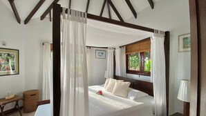 A four-poster bed with a canopy, a wooden headboard, and a window with a view of greenery.