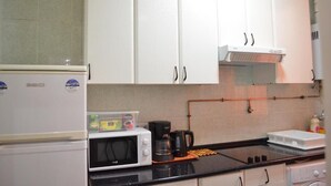 A kitchen with white cabinets, a microwave, a coffee maker, and a stove. - Rooms Barco (Madrid)
