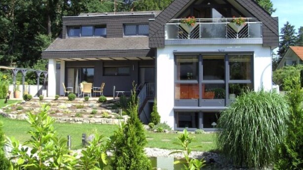 Une maison à deux étages avec un balcon, un jardin et un étang.