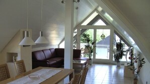 Un espace repas comprenant une table et des chaises en bois, un canapé en cuir marron et une grande fenêtre donnant sur un paysage verdoyant.