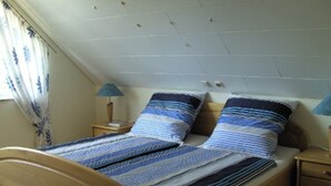 Une chambre avec un plafond en pente, deux tables de chevet avec des lampes, un lit avec une literie à rayures et une fenêtre avec des rideaux.