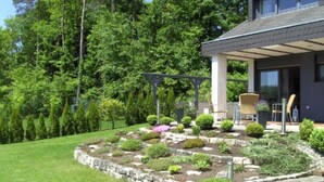 Une maison moderne dotée d’un patio couvert, d’un jardin avec différentes espèces de plantes et d’une pelouse.