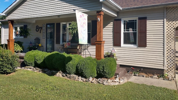 A two-story house with a welcoming front porch, a mailbox, and a number 87 sign.