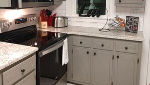 A kitchen with grey cabinets, a stainless steel microwave, a stove, and a window with a view.