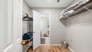 A narrow hallway with a wooden floor, a white door, a metal rack with clothes, and a small basket. - Life's a Breeze | 5min to Pcola Beach • Families (Gulf Breeze)