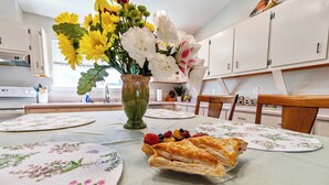 A dining table with floral placemats, a vase with flowers, and a plate of food. - Life's a Breeze | 5min to Pcola Beach • Families (Gulf Breeze)