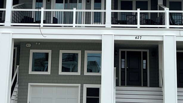 En toetagers bygning med balkon på øverste etage, garage i stueetagen og et tydeligt synligt adressenummer.
