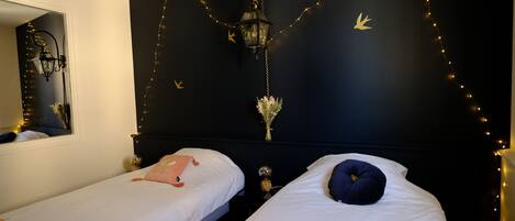 Een slaapkamer met twee bedden, een spiegel, lichtjes en een wandlamp.