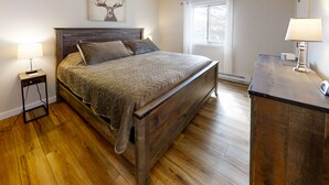 A bedroom with a wooden bed, a nightstand with a lamp, and a window with curtains.