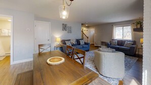 A spacious living room with a wooden dining table, two sofas, and a staircase leading to another level.