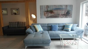 Una sala de estar con un sofá modular, una mesa de centro de vidrio y un cuadro en la pared.