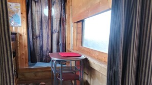 A compact RV interior with a wooden interior, a small table with a red placemat, metal chairs, and a window with curtains. - Stone cottage@ La loma del chivo (Marathon)