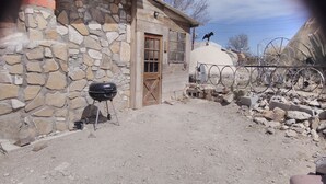 A rustic outdoor area with a stone wall, a wooden door, a barbecue grill, and a bicycle wheel fence. - Stone cottage@ La loma del chivo (Marathon)