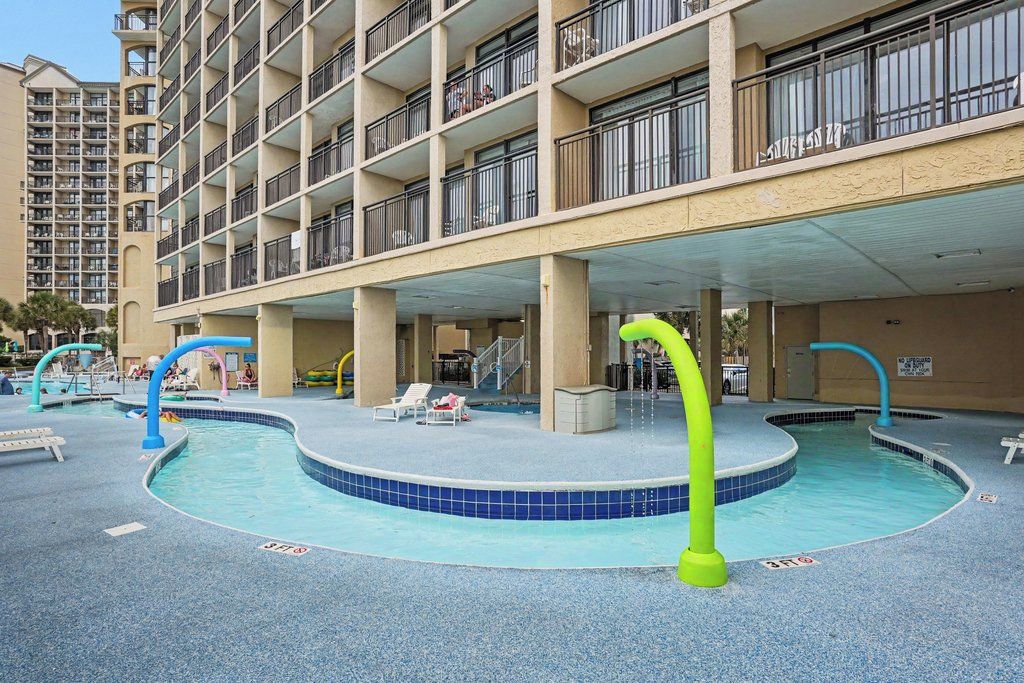 Un hotel con varios balcones, un área de piscina con sillones de descanso y un paseo cubierto.