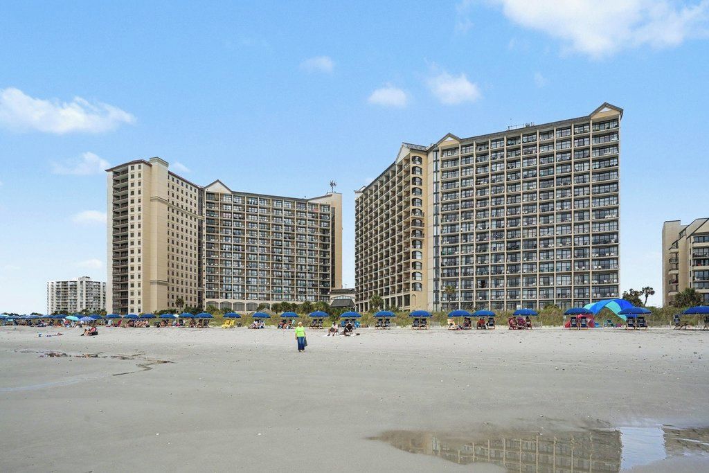 Un hotel frente a la playa con varios edificios altos, una playa de arena y sombrillas.