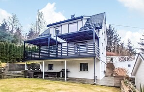 Ett tvåvåningshus med en balkong, en inglasad veranda och en liten trädgård.