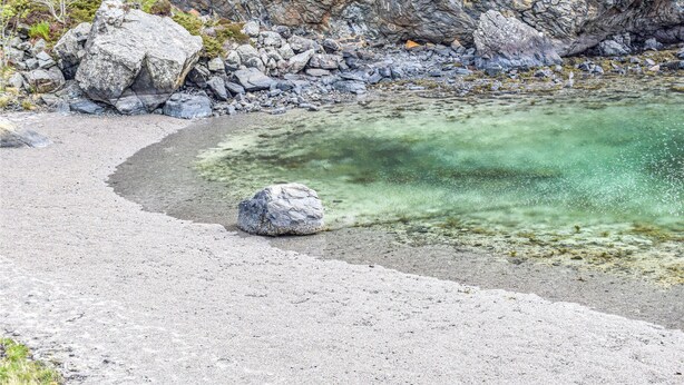 A rocky shoreline with clear water, a gravel path, and a large boulder in the foreground. - Amazing apartment in Fjell with WiFi (Fjell)
