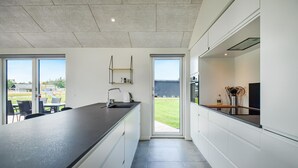 A modern kitchen with a large island, a sink, and a dining area with chairs. There is a view of a playground outside. - Luxurious home in Glesborg with WiFi (Glesborg)