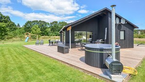 A modern outdoor deck with a hot tub, barbecue grill, and a wooden play structure. - Luxurious home in Glesborg with WiFi (Glesborg)