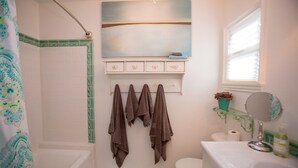 A bathroom with a bathtub, toilet, sink, and a mirror. There are towels hanging on a rack and a potted plant on the windowsill. - Santa Monica Beach Luxury Suite (Santa Monica)
