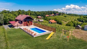A pool area with a slide, a wooden deck, and a view of a vineyard and houses in the background.