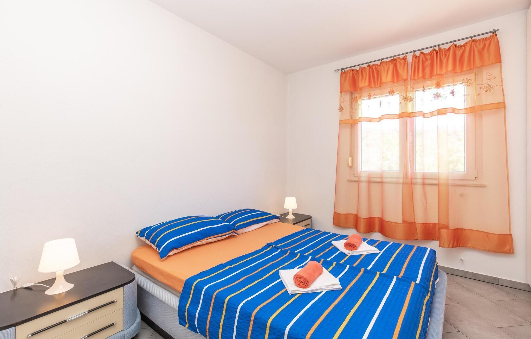 A bedroom with a bed, two bedside tables, a lamp, and a window with curtains.