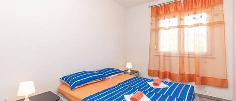 A bedroom with a bed, two bedside tables, a lamp, and a window with curtains.