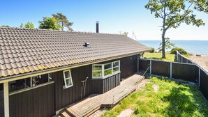 Eine Holzhütte mit einem Ziegeldach, großen Fenstern und einer Terrasse mit Blick auf einen Strand.