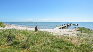 Ein Strand mit einer Holzstege, der sich über ruhiges Wasser erstreckt, einem Sandstrand und einer Person, die am Sand sitzt.