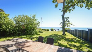 Eine Holzterrasse mit Gartenmöbeln und Blick auf das Meer, sowie eine Fahnenstange.