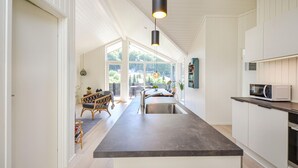 A modern kitchen with a central island, white cabinetry, and a view to a patio area. - Beautiful home in Ebeltoft with kitchen (Ebeltoft)