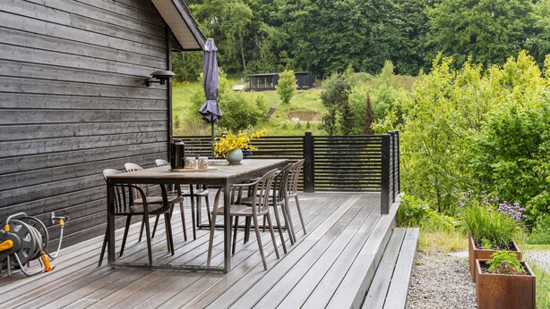 A wooden deck with a table and chairs, a hose reel, and a garden with plants and flowers. - Beautiful home in Ebeltoft with kitchen (Ebeltoft)
