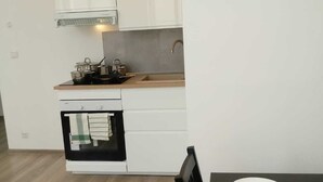 Cuina moderna amb armaris blancs, forn de sobre i zona de menjador amb taula per a dues persones.