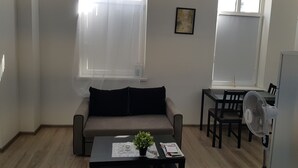 Un saló amb un sofà, una taula baixa amb una planta, una taula de menjador amb caires i un ventilador de peu.