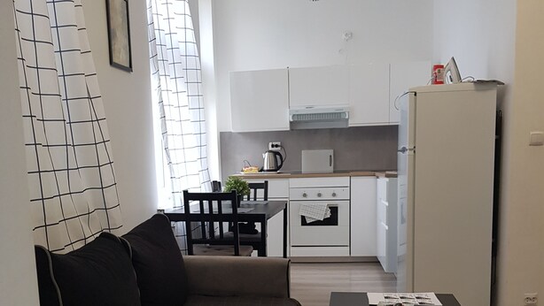 Un saló modern amb un sofà i una taula de centre, una cuina amb armaris i electrodomèstics blancs, i una zona de menjador amb caires i una taula.