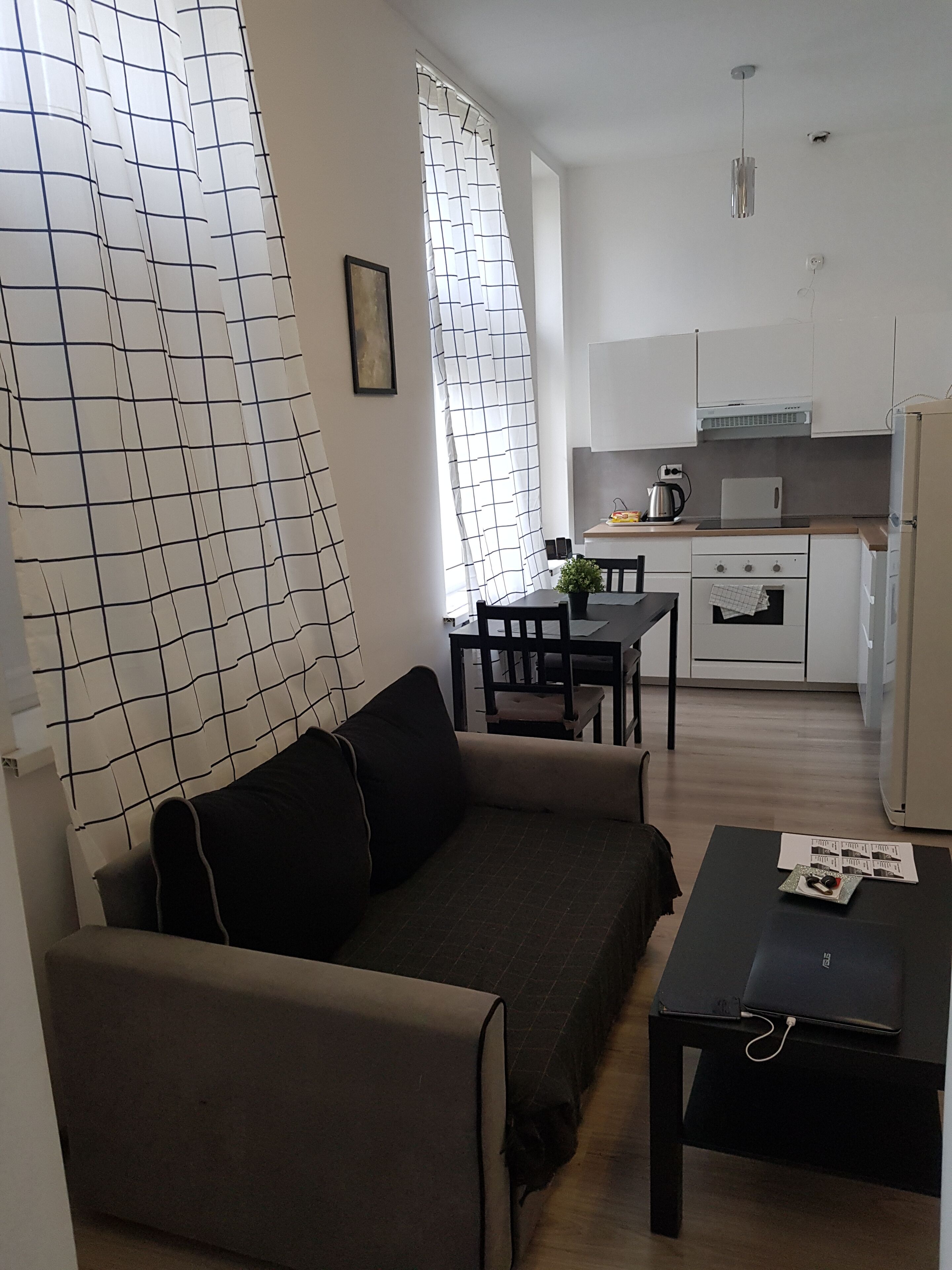 A modern living room with a sofa, a coffee table, and a dining area with a table and chairs. There is a kitchen area with a microwave, stove, and cabinets.