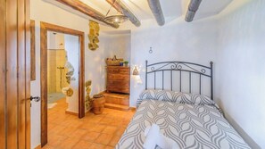 Een slaapkamer met een bed, een houten dressoir en een stenen muur.