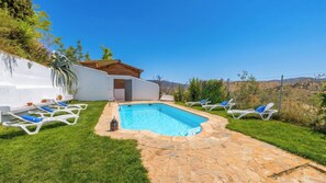 A swimming pool with lounge chairs, a stone pathway, and a white building with a wooden roof. - Dehesa de las Casas Algarinejo by Ruralidays (Granada)