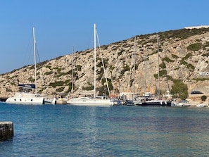 A marina with several sailboats docked, rocky hills in the background, and a clear blue sky.
