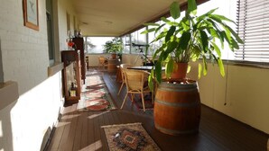 A covered outdoor area with a wooden floor, a large potted plant, wicker chairs, and a table. - Leconfield House, the heart of the Hunter Valley, built 1872, 150yrs in 2022 (Leconfield)