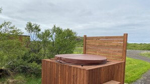 A wooden hot tub with a bench and steps, surrounded by greenery and a wooden deck.