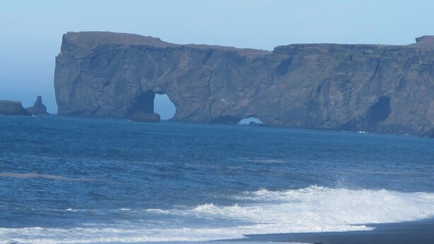 A coastal landscape with a prominent cliff featuring a natural arch formation.