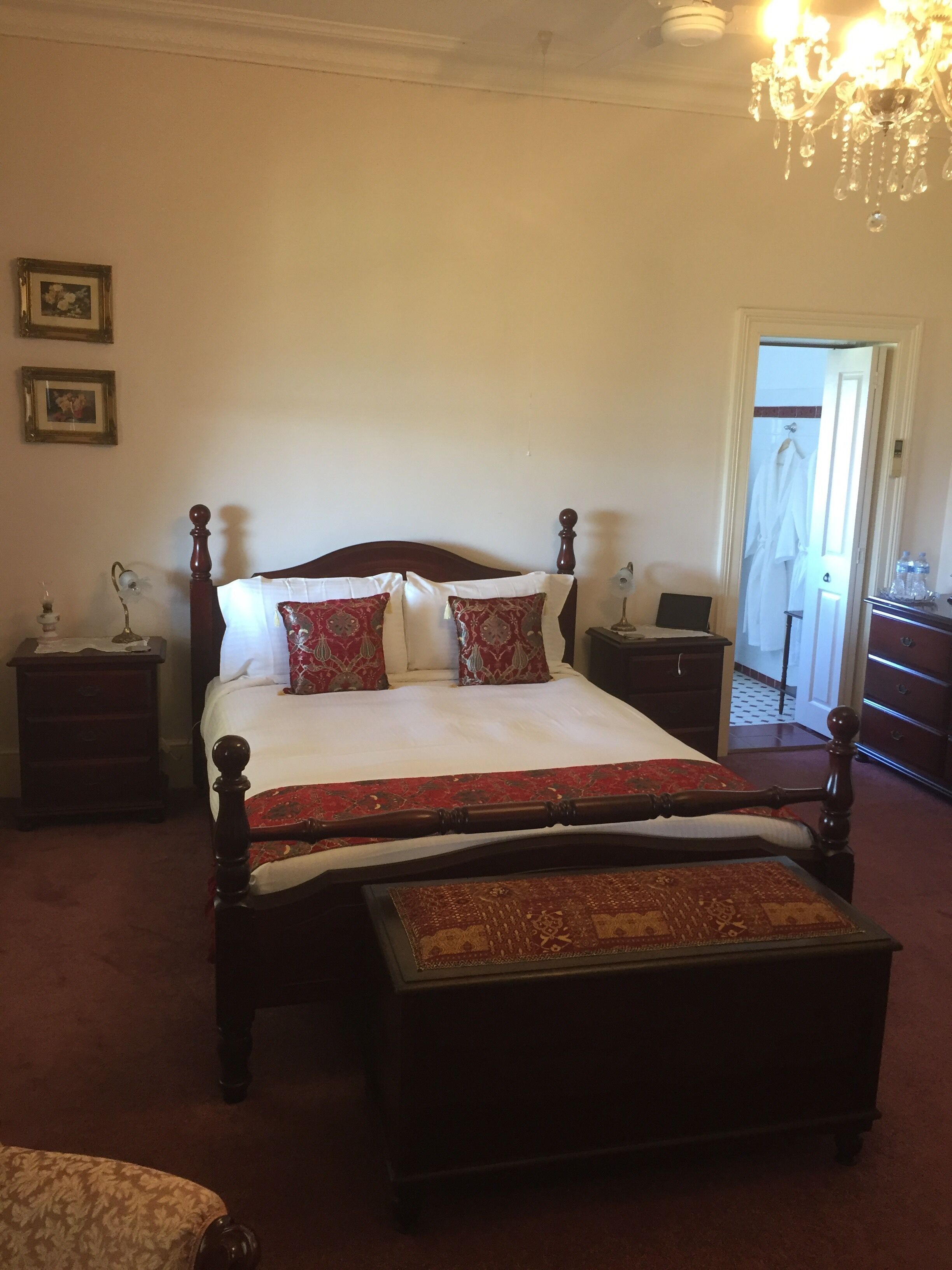 A traditional bedroom with a four-poster bed, a nightstand, a dresser, and a chandelier.
