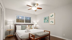 A bedroom with a bed, bedside tables, a ceiling fan, a window, and artwork on the wall.