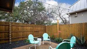 Un jardin avec une clôture en bois, trois chaises turquoise et une petite table.
