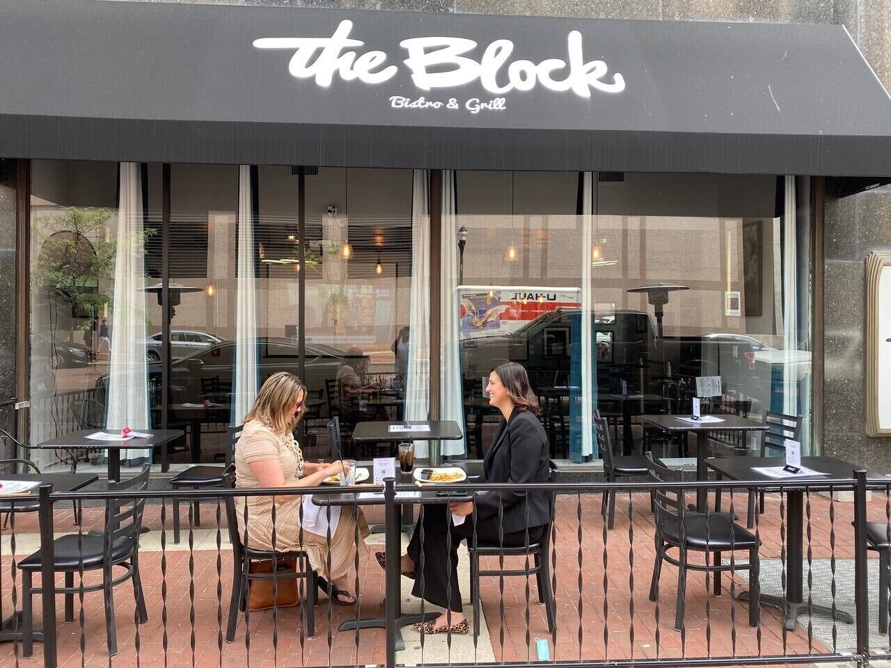 An outdoor dining area with tables and chairs, a large window, and a sign reading 'the Block Bistro & Grill'.