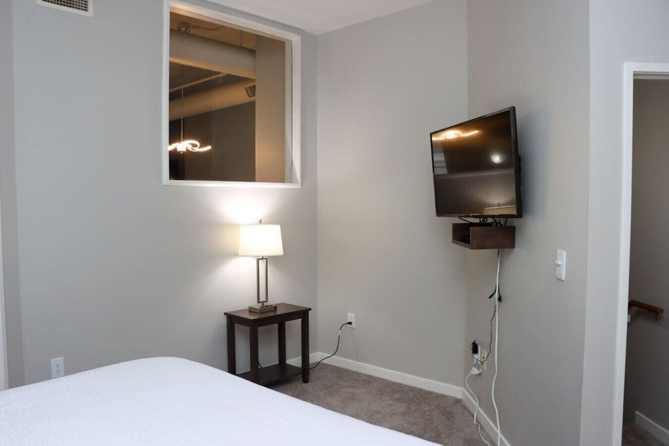 Une chambre à coucher comprenant un lit, une lampe de chevet, un téléviseur fixé au mur et une fenêtre donnant sur l’intérieur.