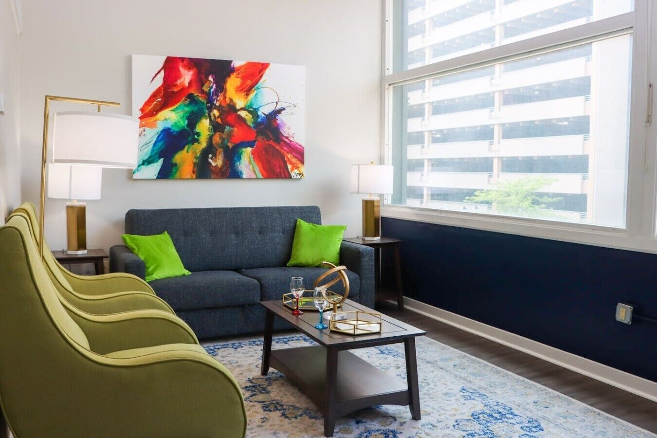 A modern living room with a sofa, green armchairs, a coffee table, and a colorful abstract painting.